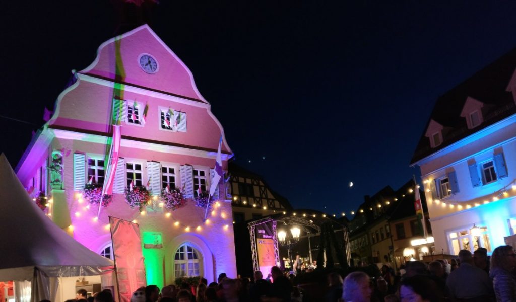 Der Mond hat sich zurückgezogen. Hier braucht man ihn nicht. Wenn sich später die Nacht über das Fest gelegt hat, wird er wiederkommen und den Menschen nach Hause leuchten.